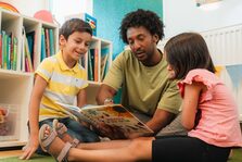 Ein Mann liest zwei Kindern ein Buch vor.