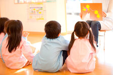 Kinderbetreuung, Kinder sitzen vor einer Betreuering, die ein Bild zeigt.